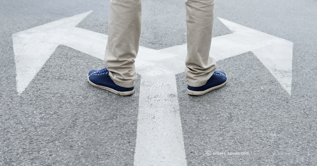 A pair of feet stand on a road in between two diverging arrows_olaser, Canva.com