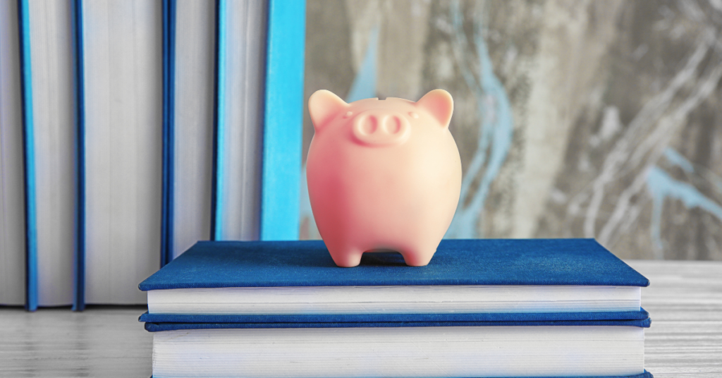 A picture of a pink piggy bank standing on blue books.
